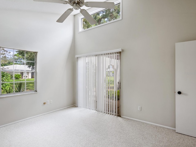 carpeted empty room with ceiling fan, a wealth of natural light, and a towering ceiling