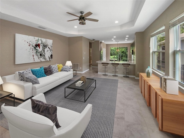 living room with ceiling fan, a tray ceiling, and light tile patterned floors