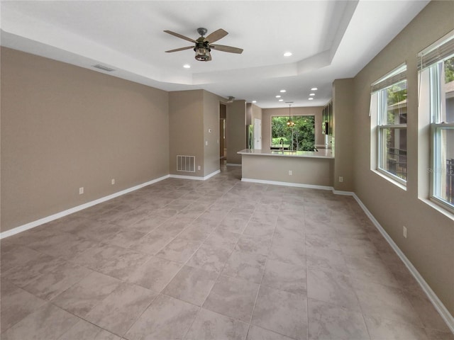 unfurnished room featuring ceiling fan, a tray ceiling, light tile patterned floors, and a healthy amount of sunlight