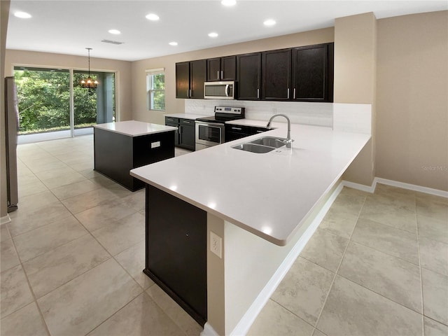 kitchen featuring a center island, decorative light fixtures, stainless steel appliances, light countertops, and a sink