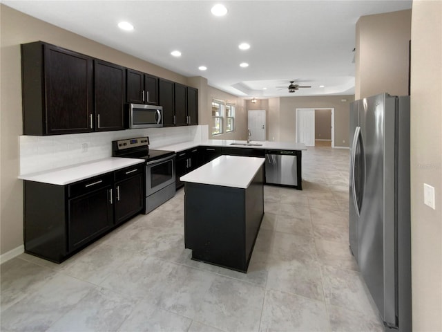 kitchen with stainless steel appliances, ceiling fan, sink, a tray ceiling, and a center island