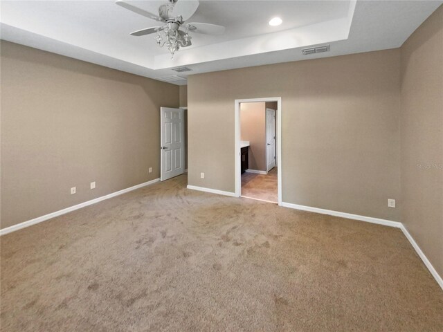 carpeted empty room with ceiling fan and a raised ceiling