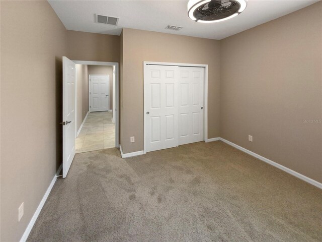 unfurnished bedroom with baseboards, visible vents, a closet, and light colored carpet