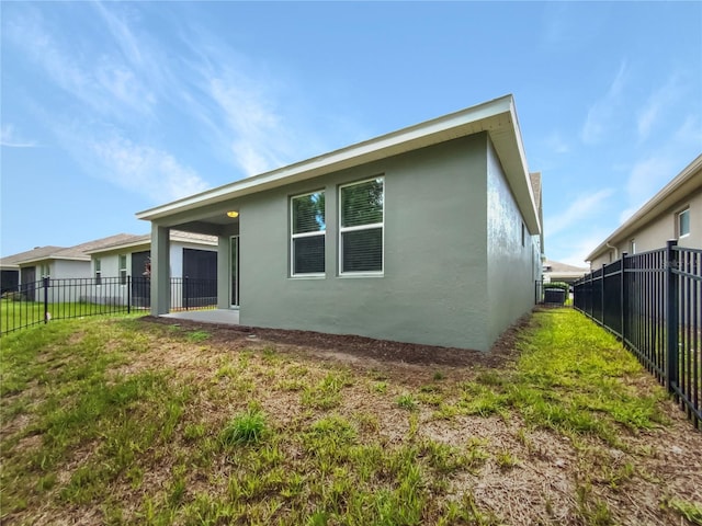 rear view of property featuring fence, a lawn, and stucco siding