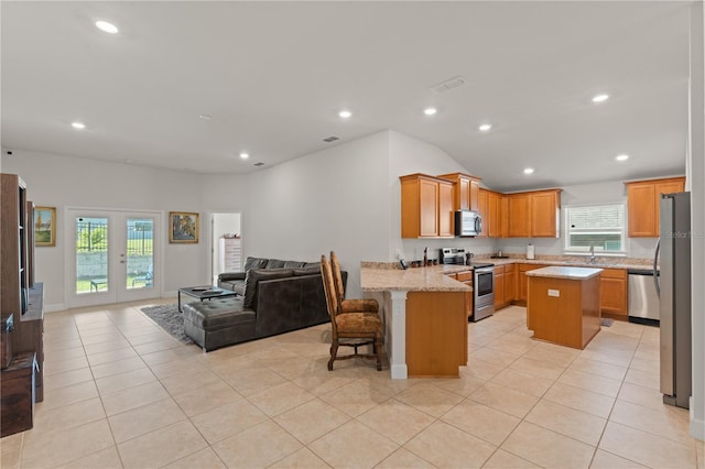 kitchen featuring stainless steel appliances, a kitchen breakfast bar, light stone countertops, kitchen peninsula, and a center island