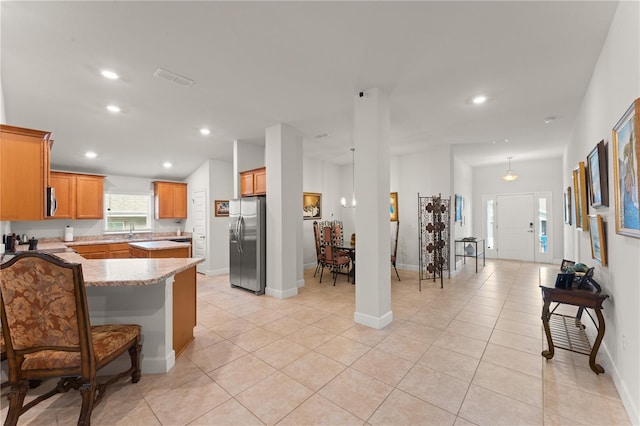 kitchen with a kitchen breakfast bar, appliances with stainless steel finishes, light stone counters, kitchen peninsula, and light tile patterned flooring