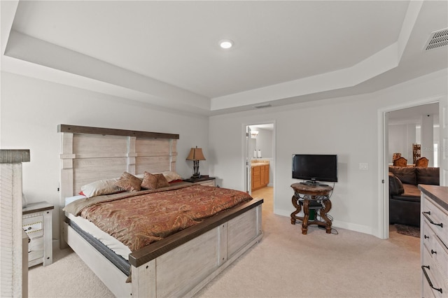 bedroom featuring ensuite bathroom, light carpet, and a tray ceiling