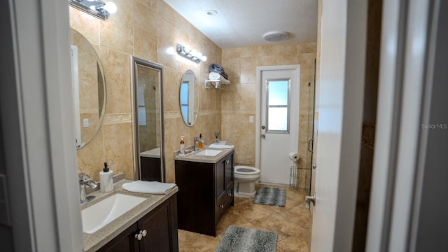 bathroom with vanity, tile patterned floors, toilet, tile walls, and a shower with shower door