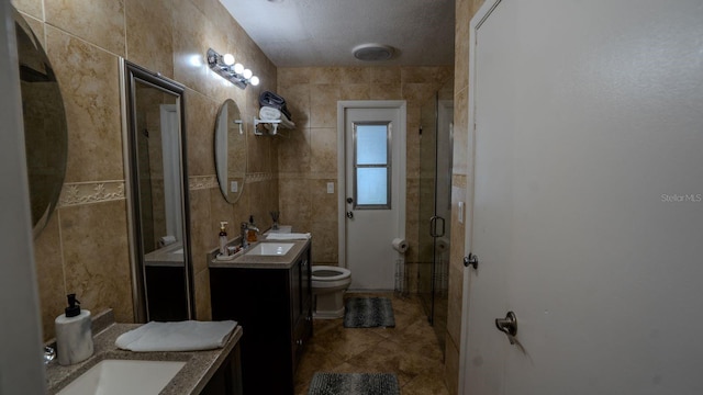 bathroom with vanity, toilet, tile walls, and walk in shower