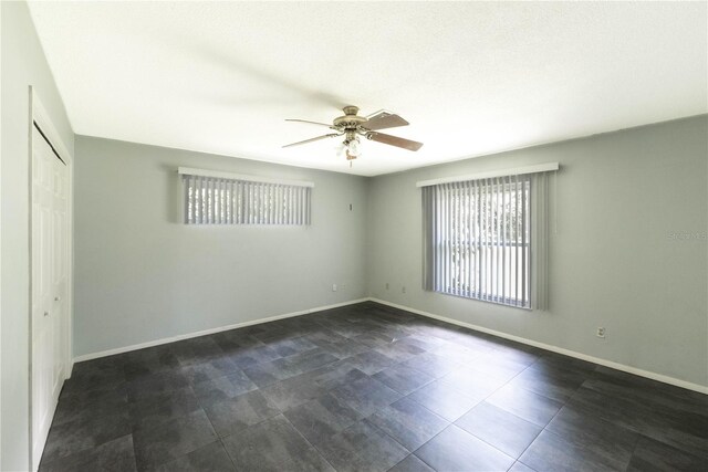 empty room with ceiling fan and dark tile patterned flooring