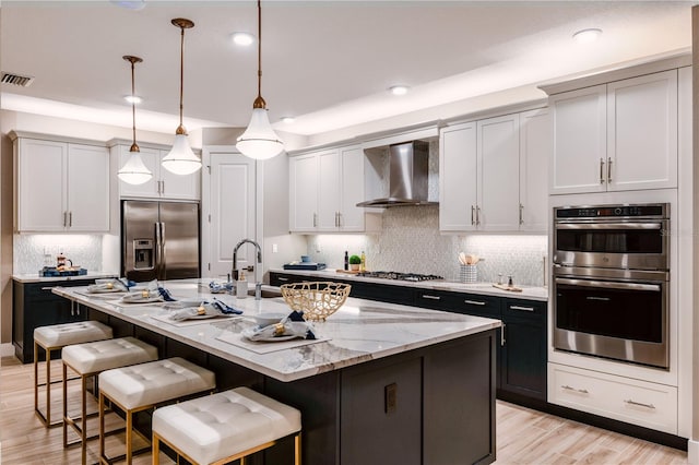 kitchen featuring stainless steel appliances, a kitchen island with sink, wall chimney exhaust hood, and tasteful backsplash