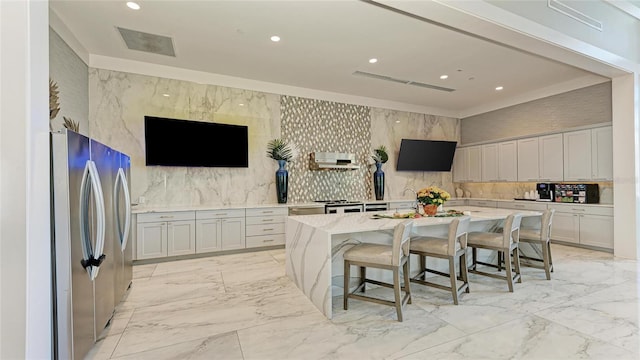 kitchen with a kitchen bar, a center island with sink, light stone countertops, light tile patterned floors, and stainless steel fridge