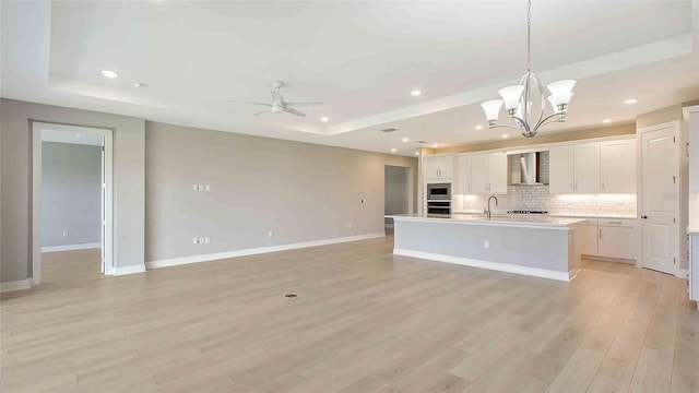 4910 Carova Way, Lakewood Ranch, FL 34211 - kitchen with wall chimney range hood, appliances with stainless steel finishes, tasteful backsplash, a tray ceiling, and a center island with sink
