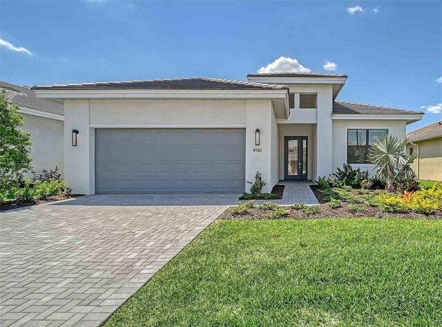 4910 Carova Way, Lakewood Ranch, FL 34211 - prairie-style home featuring a tile roof, decorative driveway, a front lawn, an attached garage, and stucco siding