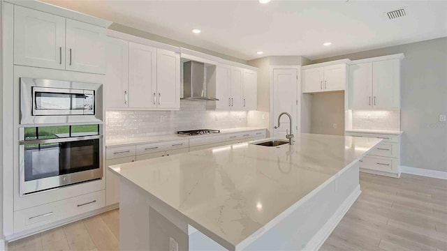 4910 Carova Way, Lakewood Ranch, FL 34211 - kitchen with a spacious island, wall chimney exhaust hood, white cabinets, a sink, and appliances with stainless steel finishes
