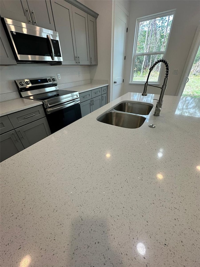 kitchen featuring gray cabinetry, sink, light stone countertops, and appliances with stainless steel finishes