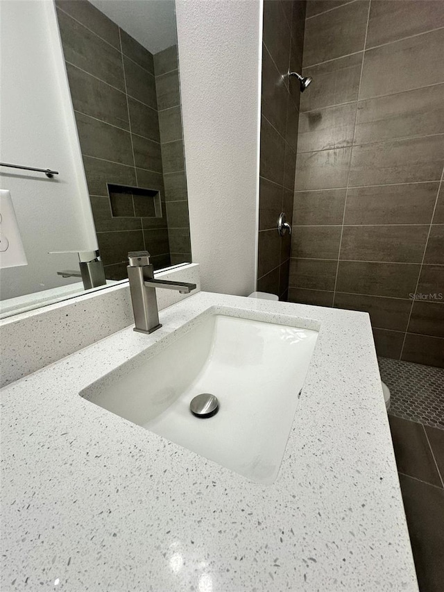 bathroom with a tile shower, vanity, and toilet