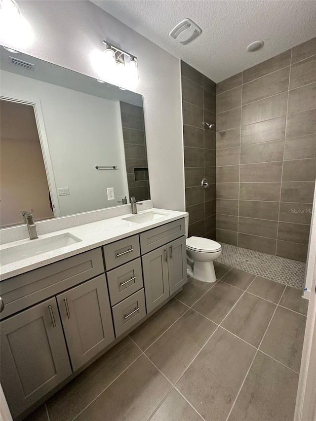 bathroom featuring vanity, tiled shower, toilet, tile patterned floors, and a textured ceiling