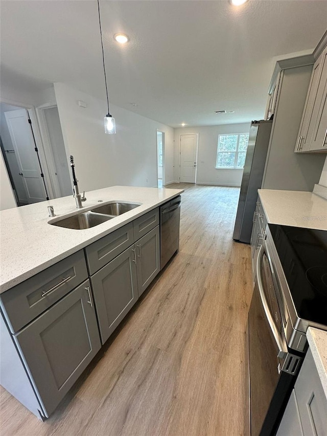 kitchen with gray cabinets, appliances with stainless steel finishes, sink, hanging light fixtures, and light hardwood / wood-style flooring