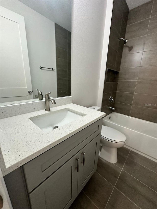 full bathroom with tile patterned flooring, tiled shower / bath, vanity, and toilet