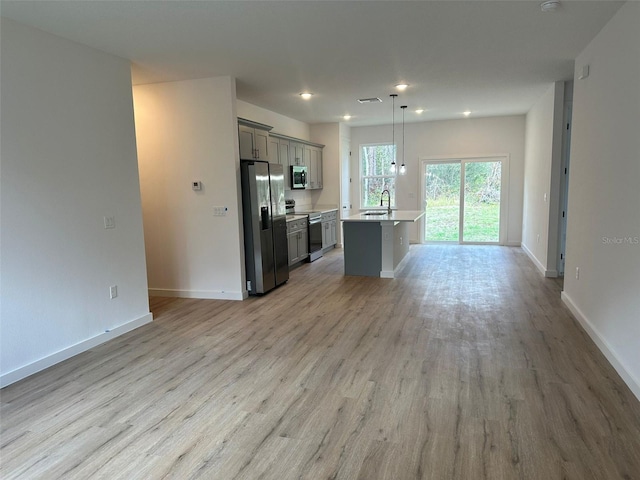 kitchen with a breakfast bar, hanging light fixtures, stainless steel appliances, light hardwood / wood-style floors, and an island with sink