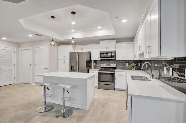 kitchen featuring stainless steel appliances, backsplash, a raised ceiling, a sink, and a kitchen island
