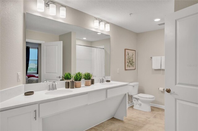 ensuite bathroom featuring baseboards, a sink, double vanity, and toilet
