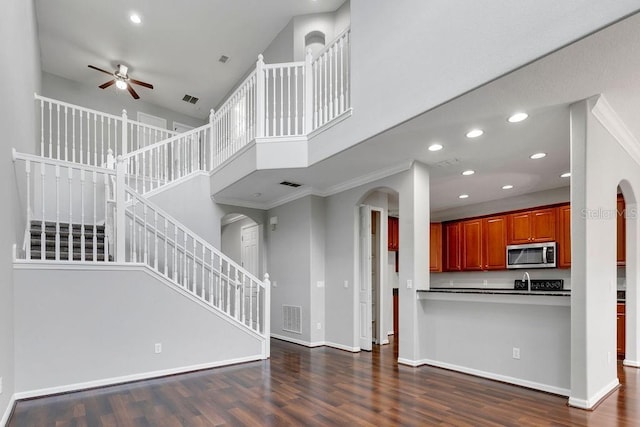 unfurnished living room featuring arched walkways, dark wood-style flooring, visible vents, a high ceiling, and baseboards