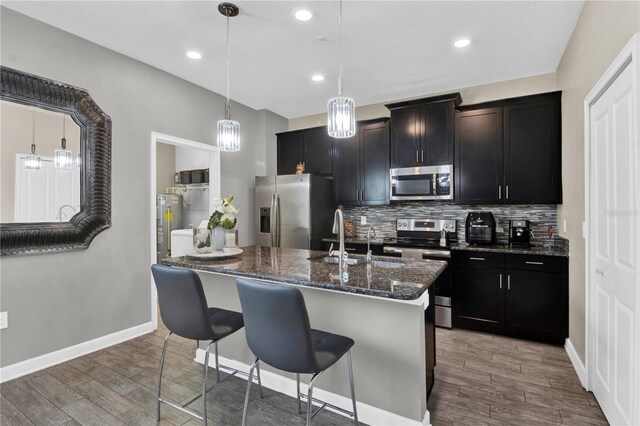 kitchen featuring sink, appliances with stainless steel finishes, hardwood / wood-style flooring, a kitchen island with sink, and tasteful backsplash