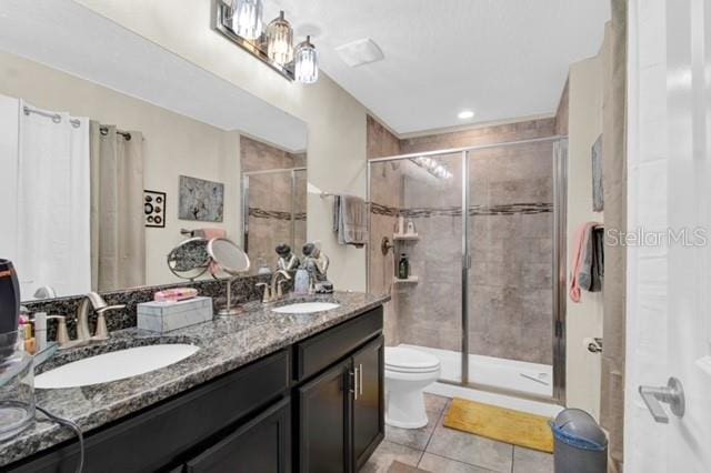 bathroom featuring toilet, dual bowl vanity, a shower with door, and tile patterned floors