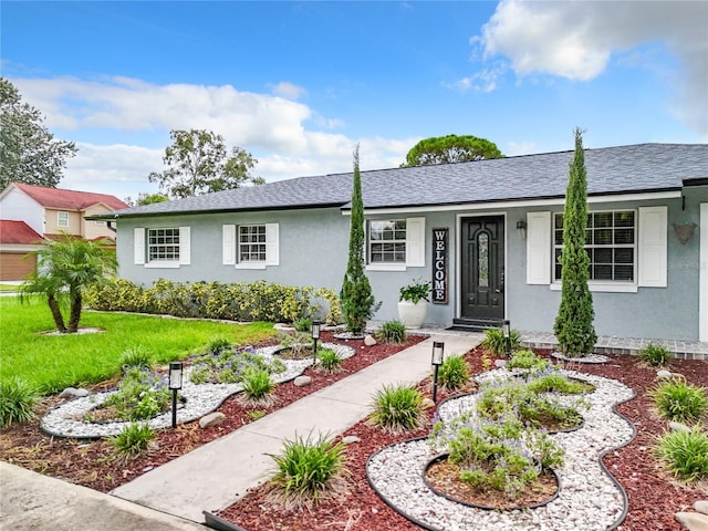 ranch-style house featuring stucco siding, roof with shingles, and a front yard