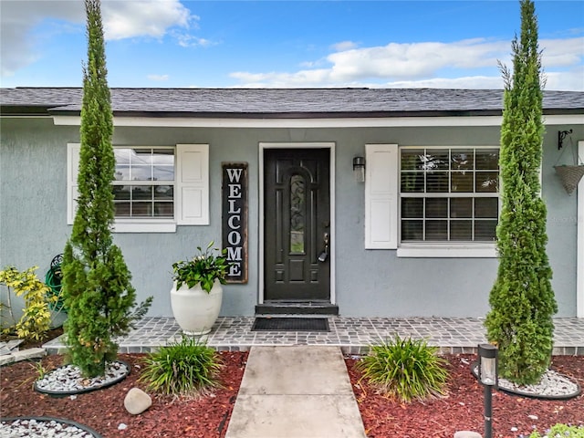 doorway to property featuring a shingled roof and stucco siding