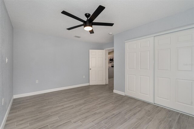 unfurnished bedroom featuring baseboards, visible vents, ceiling fan, wood finish floors, and a closet