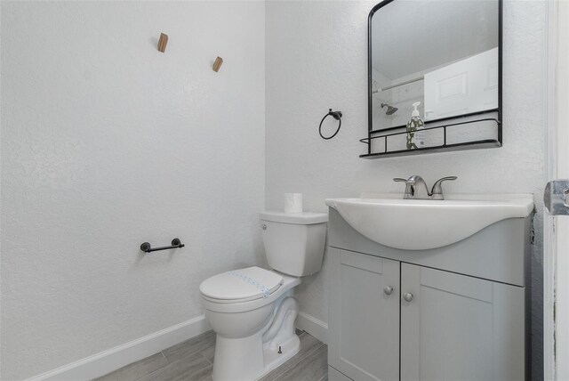 bathroom featuring toilet, wood tiled floor, baseboards, and vanity