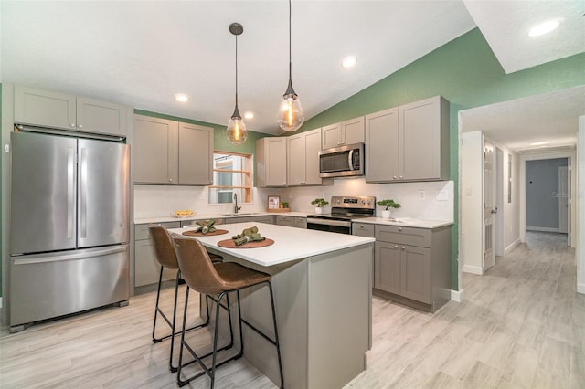 kitchen with light countertops, gray cabinetry, appliances with stainless steel finishes, vaulted ceiling, and a kitchen island