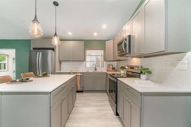 kitchen featuring appliances with stainless steel finishes, a center island, light countertops, gray cabinets, and a sink