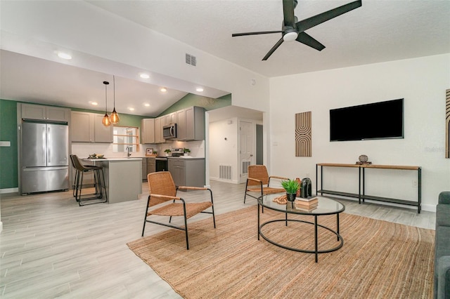 living room featuring a ceiling fan, light wood-type flooring, visible vents, and vaulted ceiling