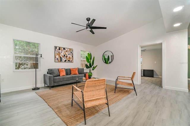 living area featuring vaulted ceiling, ceiling fan, light wood-style flooring, and baseboards