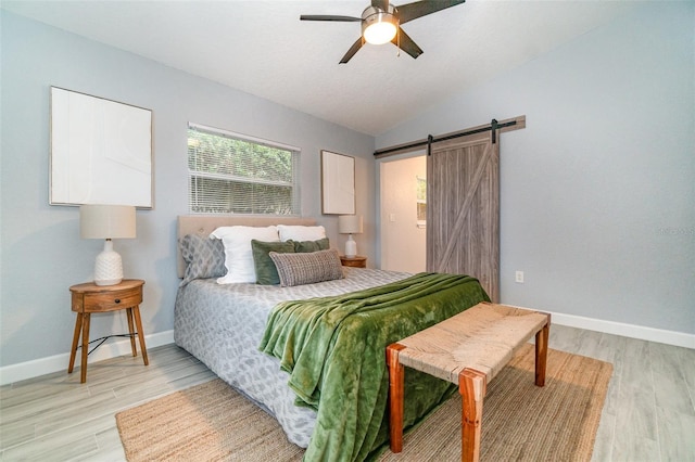 bedroom with light wood-style floors, a barn door, baseboards, and vaulted ceiling