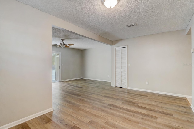 spare room with light wood-style floors, visible vents, a textured ceiling, and baseboards