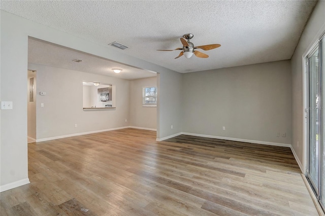 empty room featuring visible vents, light wood-style floors, ceiling fan, a textured ceiling, and baseboards