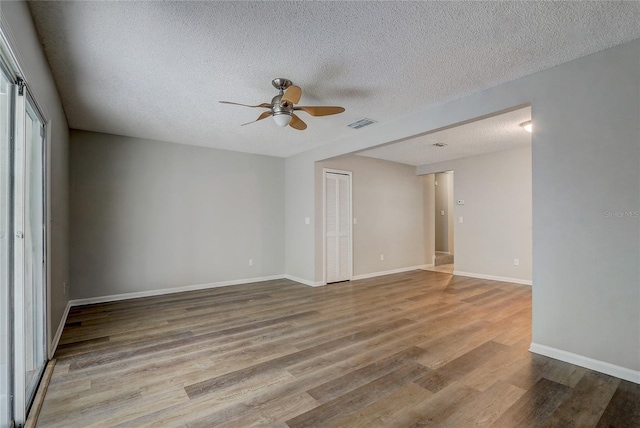 empty room with visible vents, baseboards, light wood-style flooring, ceiling fan, and a textured ceiling