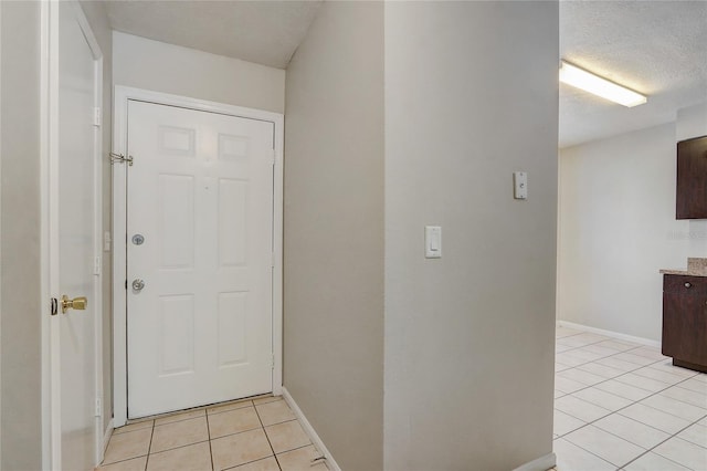 interior space with a textured ceiling, light tile patterned flooring, and baseboards