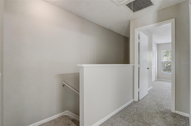 hallway featuring a textured ceiling, light carpet, an upstairs landing, visible vents, and baseboards