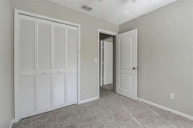 unfurnished bedroom with a textured ceiling, light colored carpet, visible vents, baseboards, and a closet