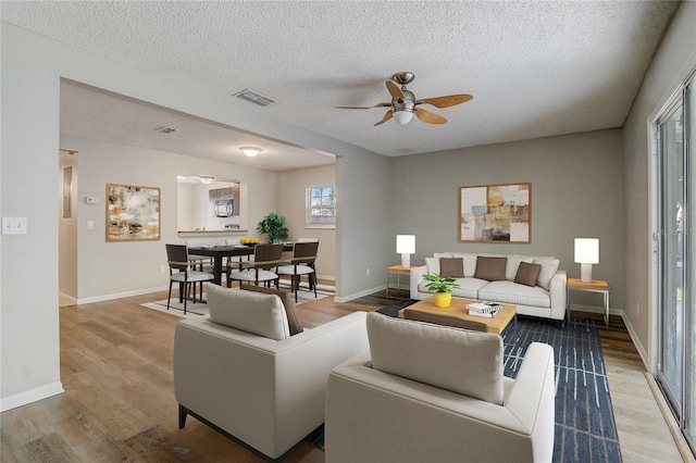 living room with visible vents, baseboards, a ceiling fan, wood finished floors, and a textured ceiling