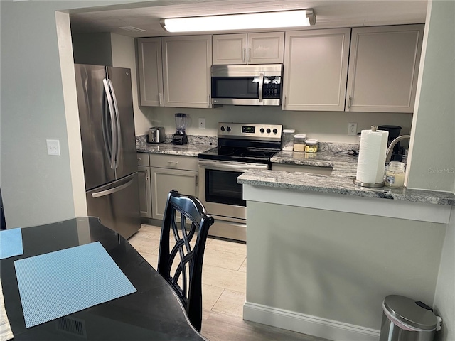 kitchen with stainless steel appliances, gray cabinets, and light stone countertops