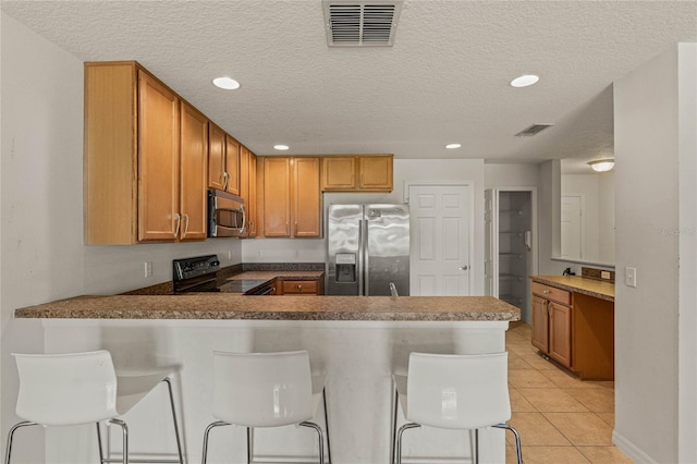 kitchen with kitchen peninsula, a kitchen bar, appliances with stainless steel finishes, and light tile patterned flooring