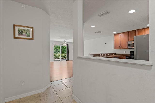 kitchen featuring ceiling fan, a textured ceiling, appliances with stainless steel finishes, and light tile patterned flooring