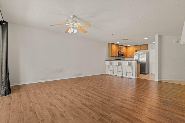 unfurnished living room featuring a textured ceiling, light hardwood / wood-style flooring, and ceiling fan